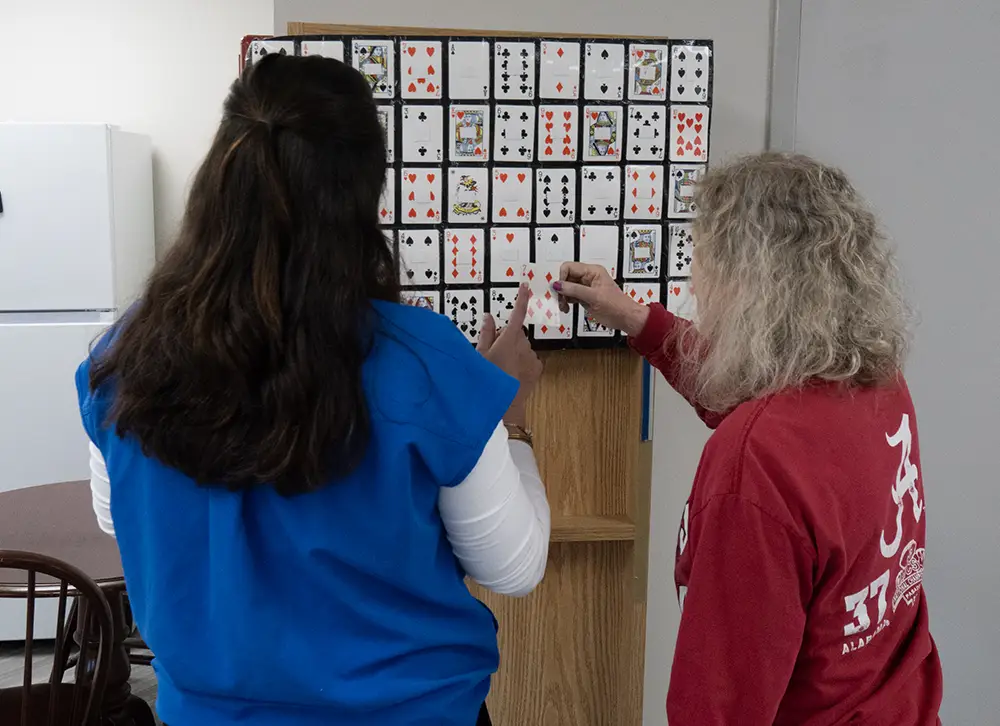 Two people stand facing a large board covered with playing cards, each pointing to a specific card.